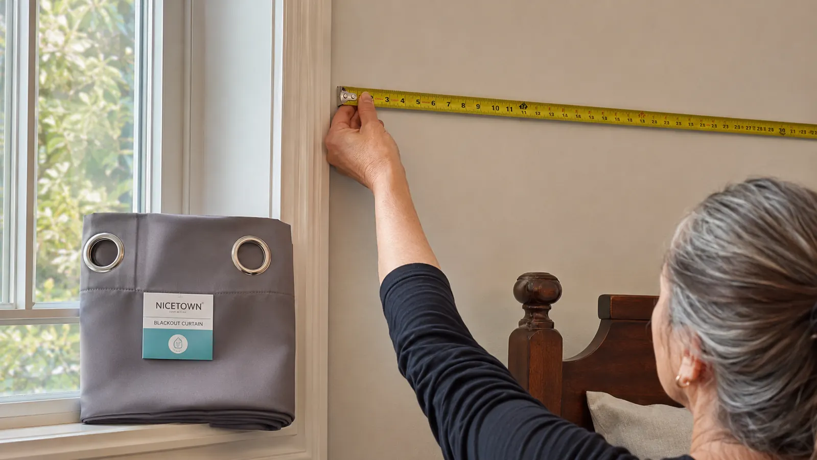 Hand holding a fabric tape measure against a window frame, extending it several inches past the edge of the frame to mark where the curtain rod brackets should go