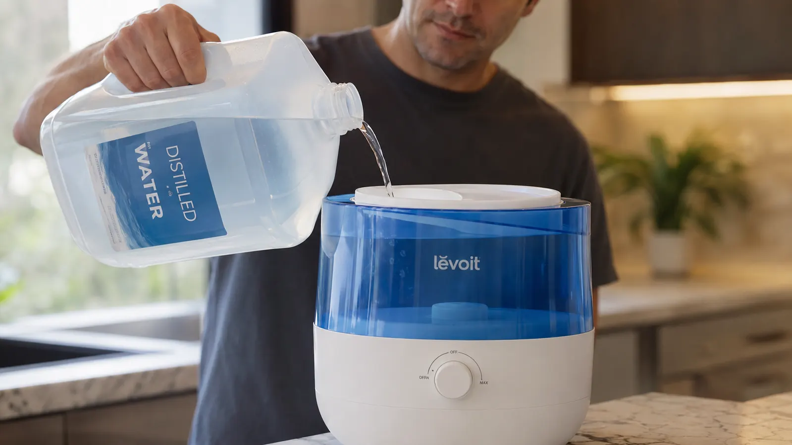 Hand pouring distilled water from a jug into the top-fill opening of the reference humidifier's tank