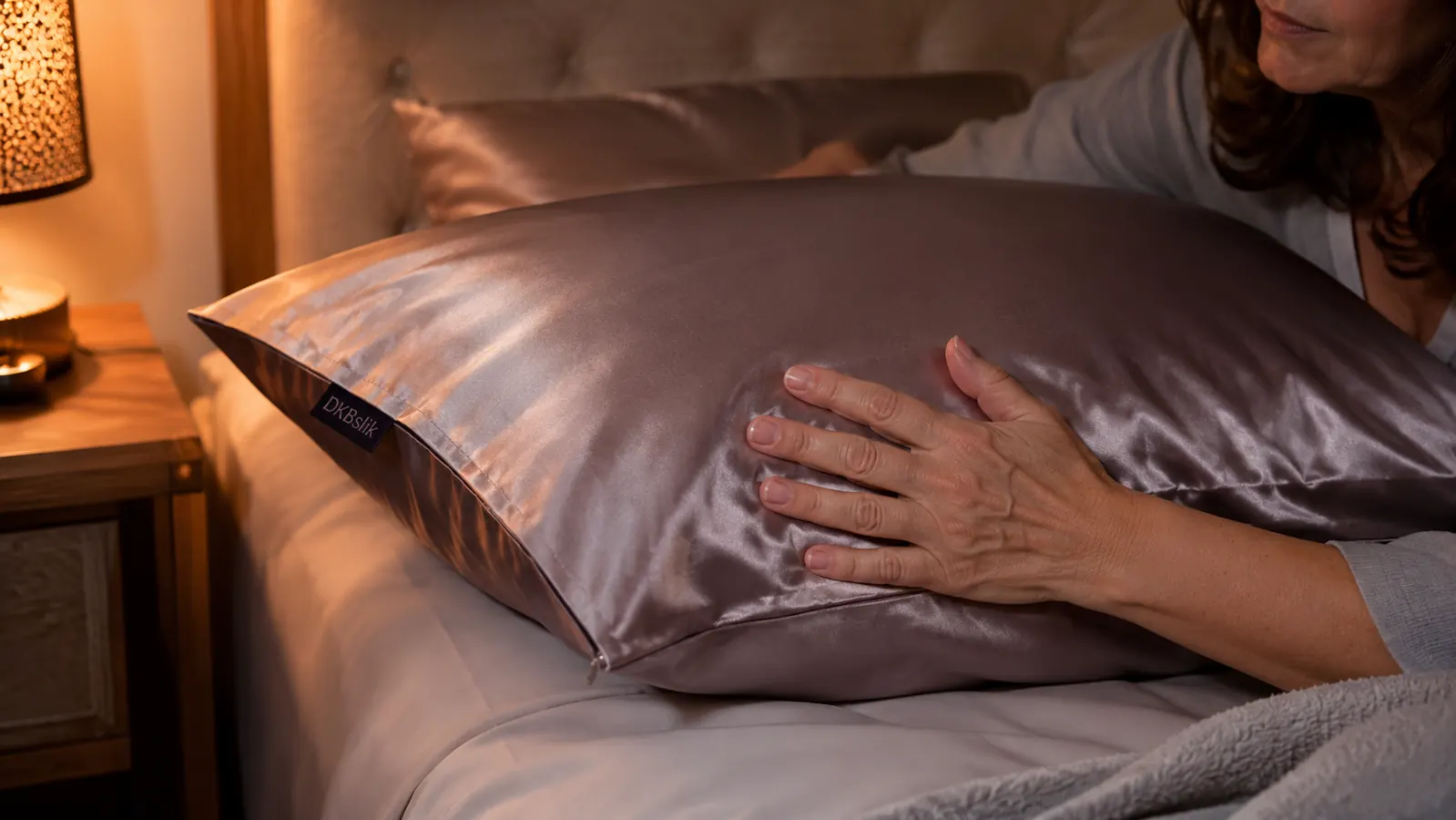 Hand smoothing a mulberry silk pillowcase over a pillow, hidden zipper closure visible at the edge