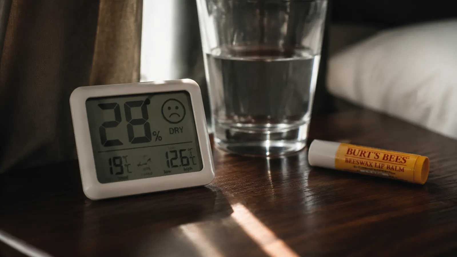 Close-up of the digital hygrometer reading twenty seven percent humidity next to a glass of water on a nightstand