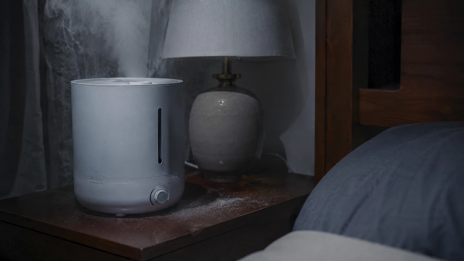 A black Levoit humidifier on a nightstand with a faint white mineral film visible on the wood surface beside it